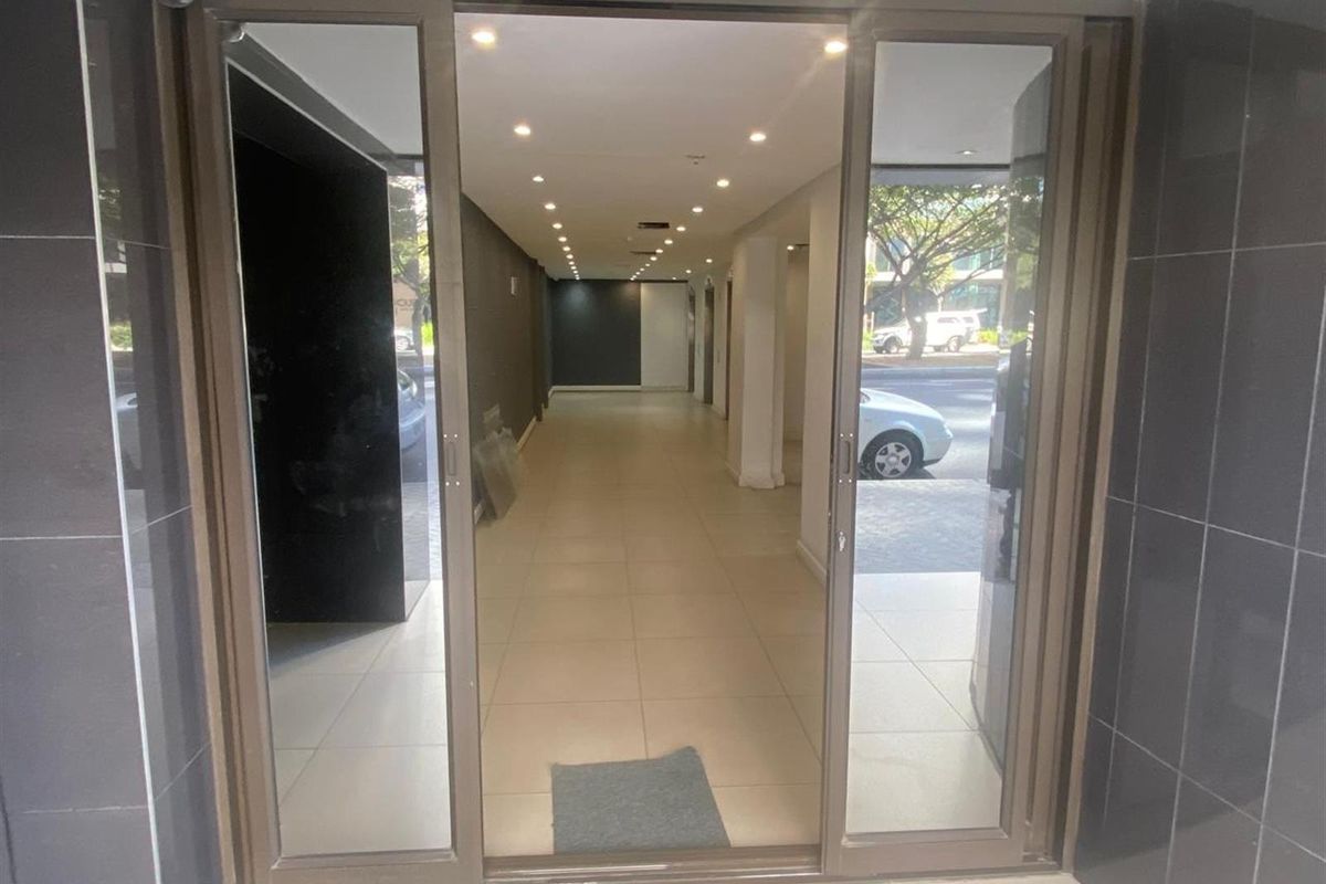 A commercial entrance featuring sliding glass doors, tiled flooring, and recessed downlighting, leading into a clean, open-plan interior space.