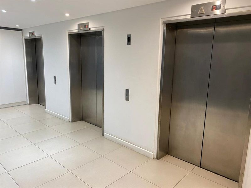 A commercial elevator lobby featuring three stainless steel lift doors and neutral tiled flooring, providing efficient vertical access within the building.