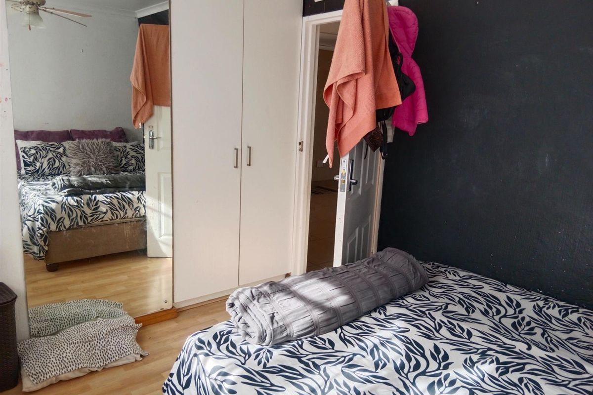 A bedroom featuring built-in cupboards with mirrored doors, laminate flooring, and a dark accent wall.