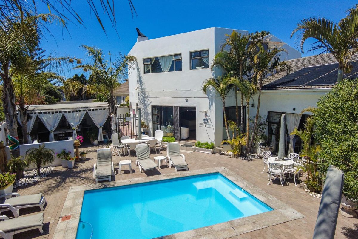 Rear exterior view featuring a swimming pool, paved patio area, and multi-level building structure with integrated solar panels.
