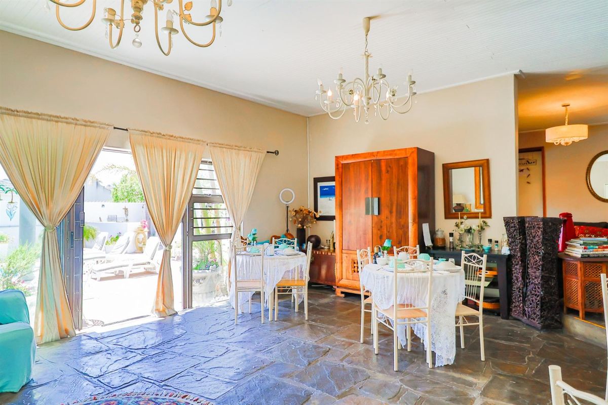 Spacious living area featuring natural stone flooring, dual chandeliers, and large sliding glass doors providing direct access to the outdoor patio.