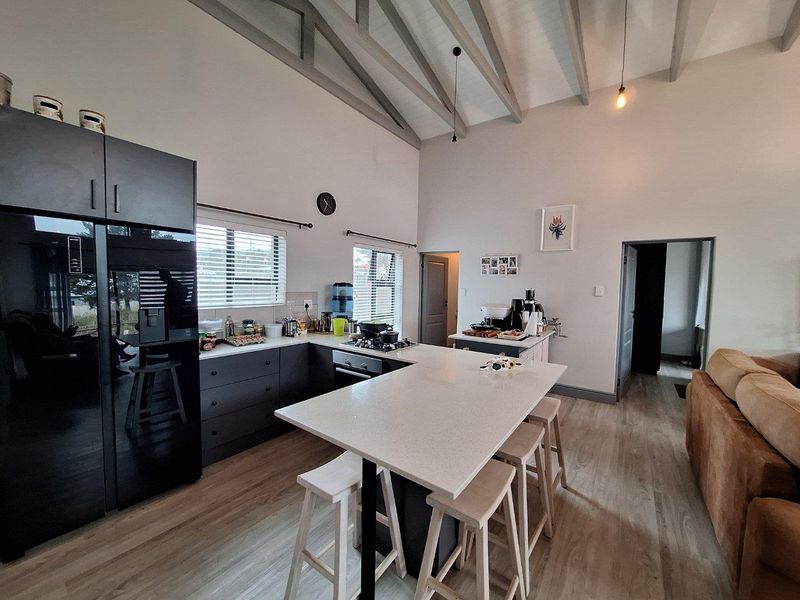 Modern open-plan kitchen featuring dark cabinetry, stone countertops, a breakfast bar, and high vaulted ceilings with exposed beams.