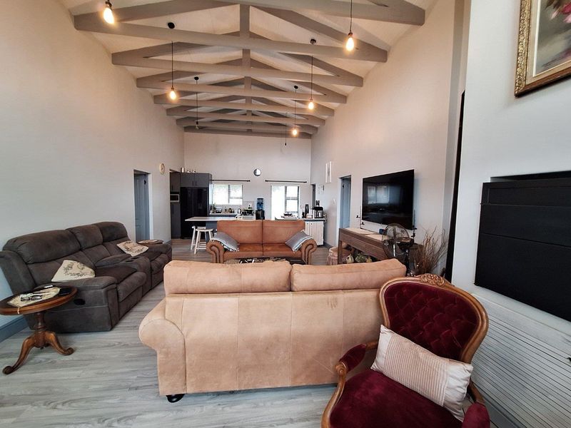 Spacious open-plan living area featuring high vaulted ceilings with exposed beams, integrated kitchen, and modern light-toned flooring throughout.