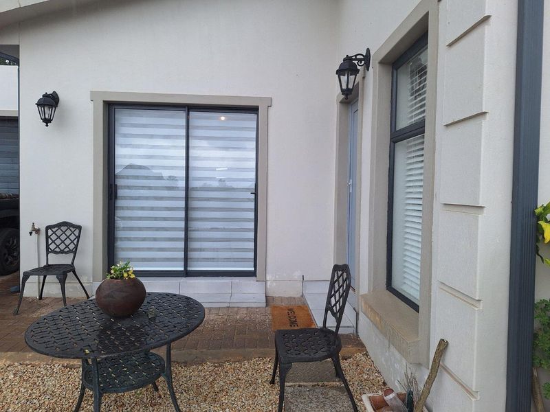A paved patio area featuring sliding glass doors, exterior wall-mounted lighting, and a window with fitted blinds.