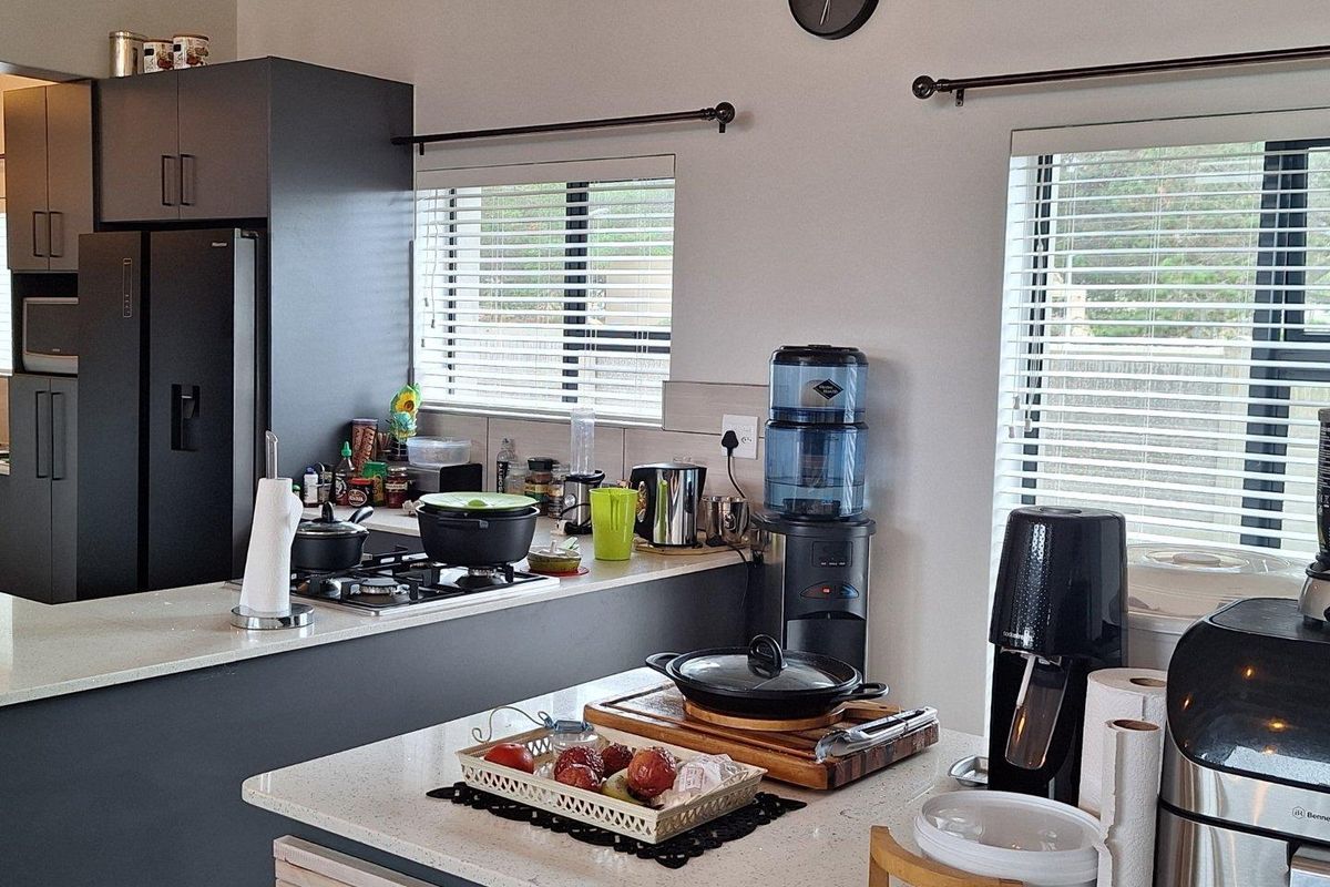 Modern kitchen featuring dark cabinetry, stone countertops, a built-in gas hob, and dual windows with fitted blinds.