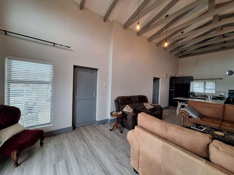 Spacious open-plan living area featuring high vaulted ceilings with exposed beams, modern wood-look flooring, and a seamless transition to the kitchen space.