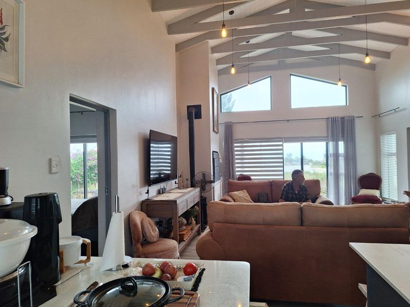Spacious open-plan living area featuring high vaulted ceilings with exposed beams, a built-in fireplace, and large windows providing ample natural light.
