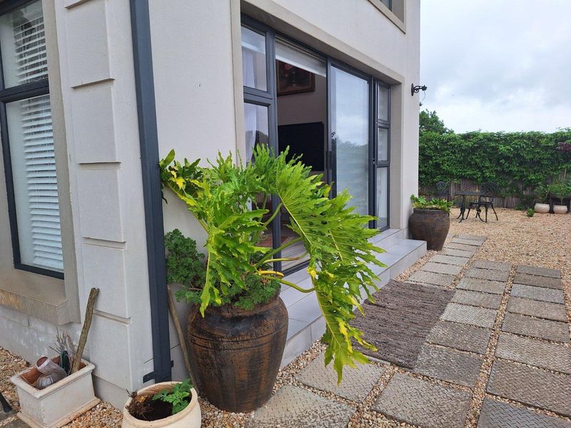 A view of the rear exterior of the house featuring a paved patio area, sliding glass doors, and landscaped garden surroundings.