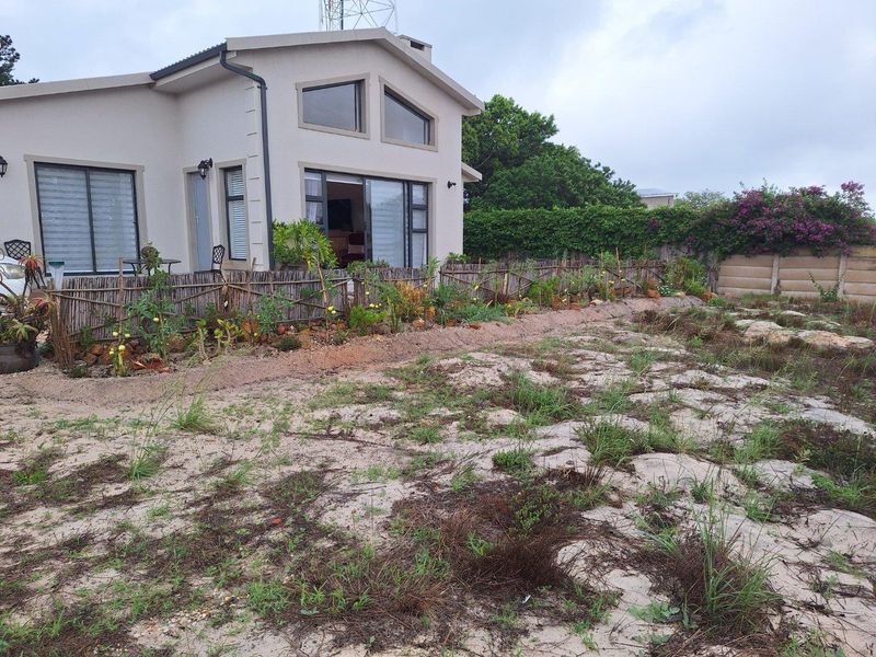 Rear view of the property featuring a modern house with large windows, sliding doors, and an expansive, natural garden area.