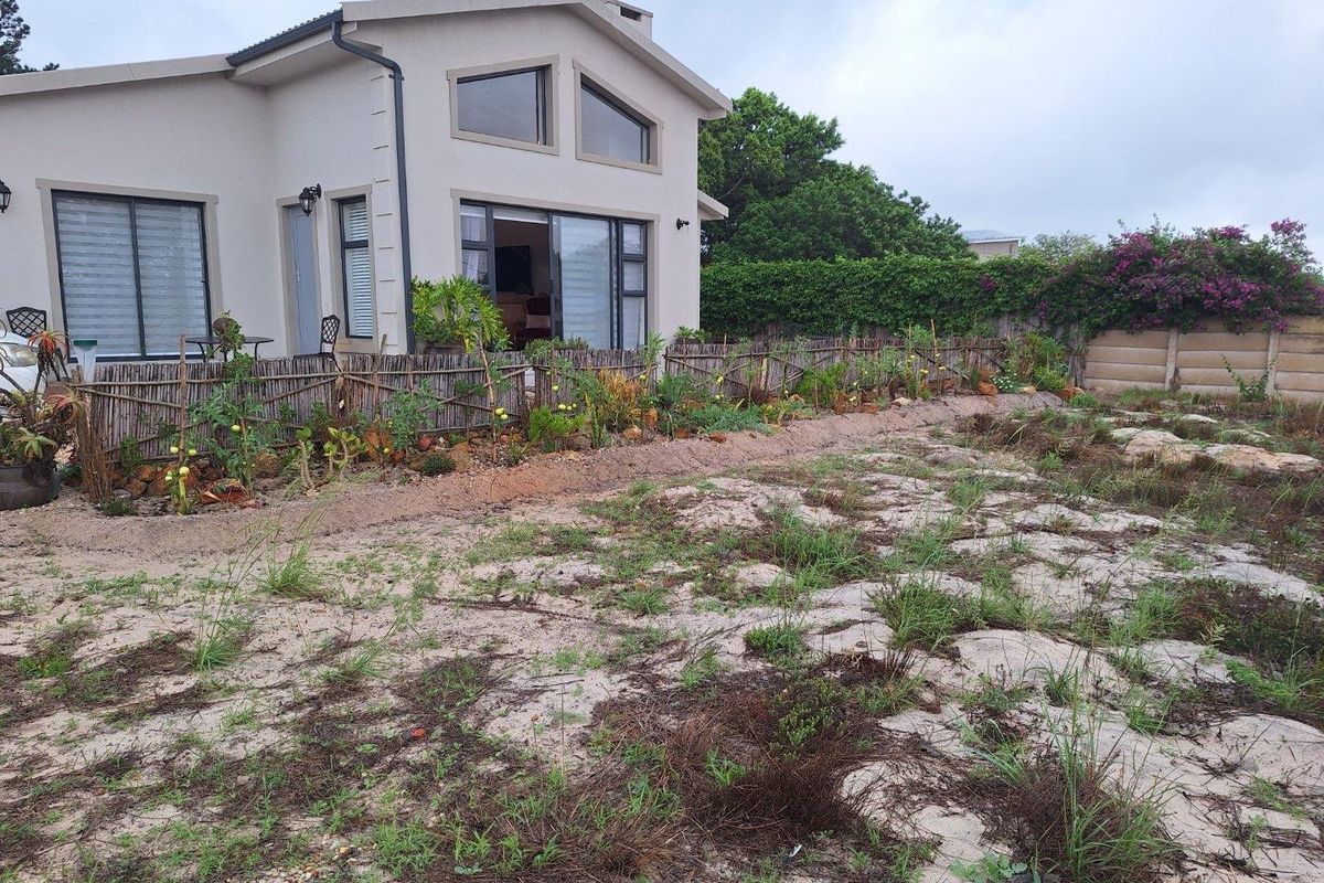 Rear view of the property featuring a modern house with large windows, sliding doors, and an expansive, natural garden area.