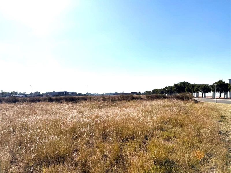 A wide-angle view of a vacant commercial land plot featuring dry grass and surrounding neighborhood infrastructure.