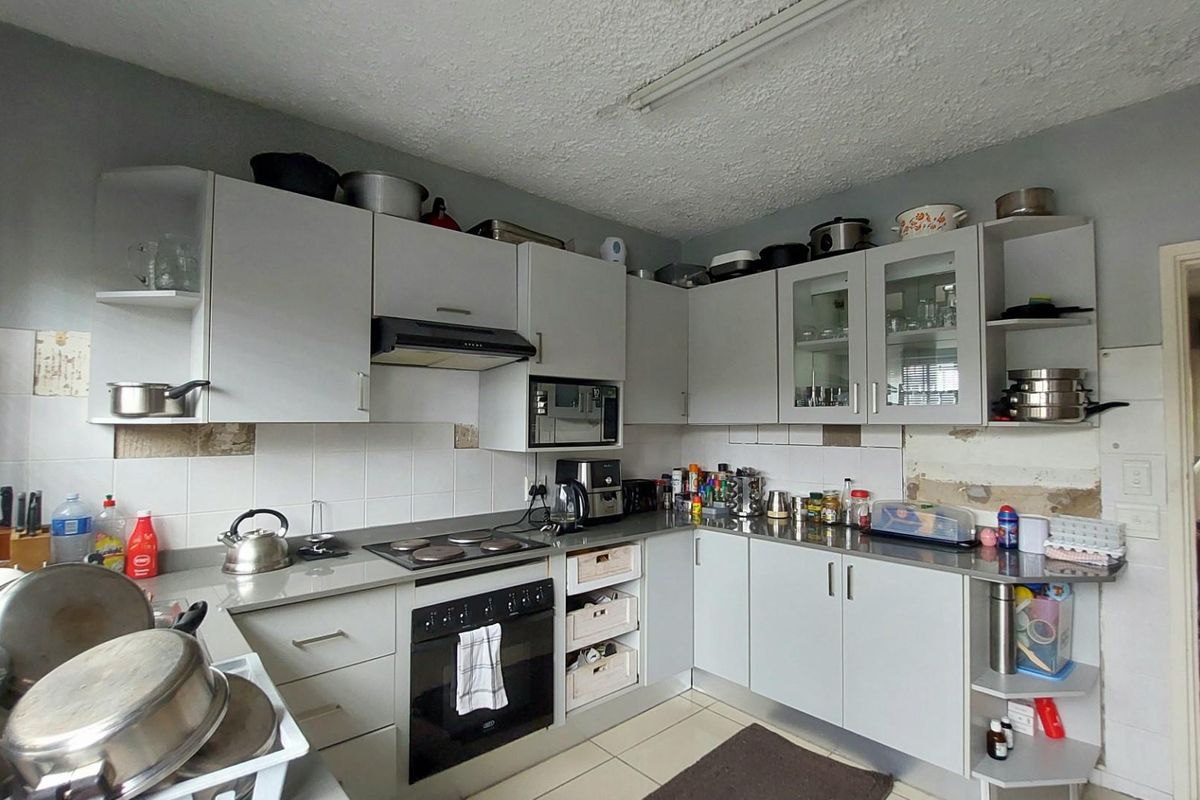 A functional kitchen featuring grey cabinetry, a built-in oven, and hob, requiring some cosmetic attention to wall tiling and plasterwork.