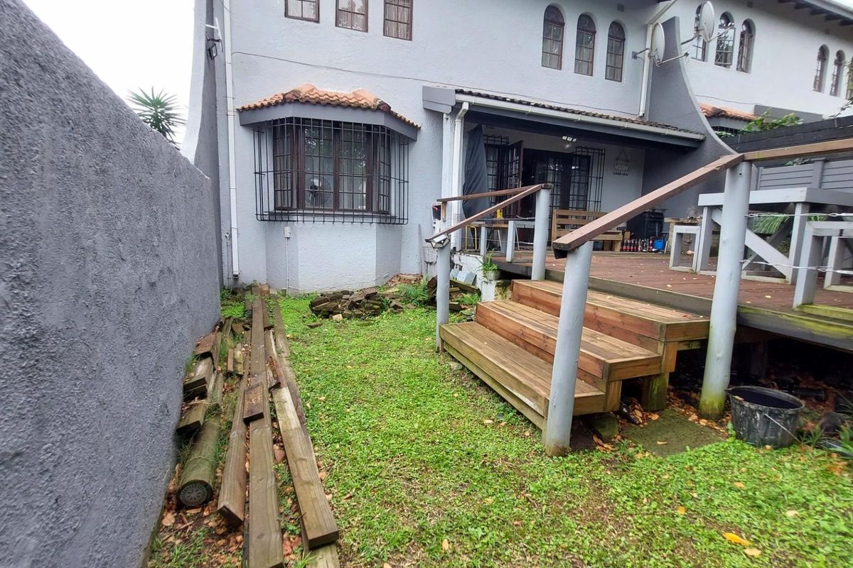 Rear view of the apartment featuring a raised timber deck, stairs, and a small garden area requiring maintenance.