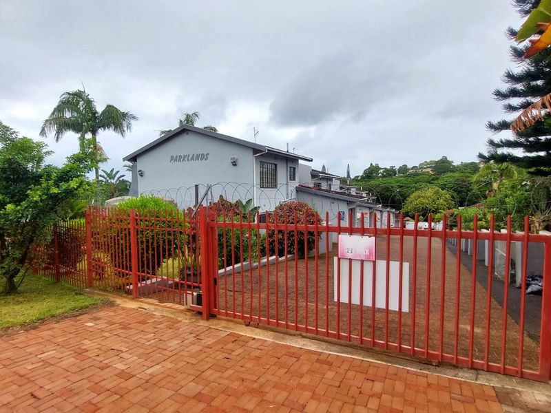 Exterior view of the Parklands apartment complex entrance, featuring a paved driveway, red metal security gate, and perimeter fencing.