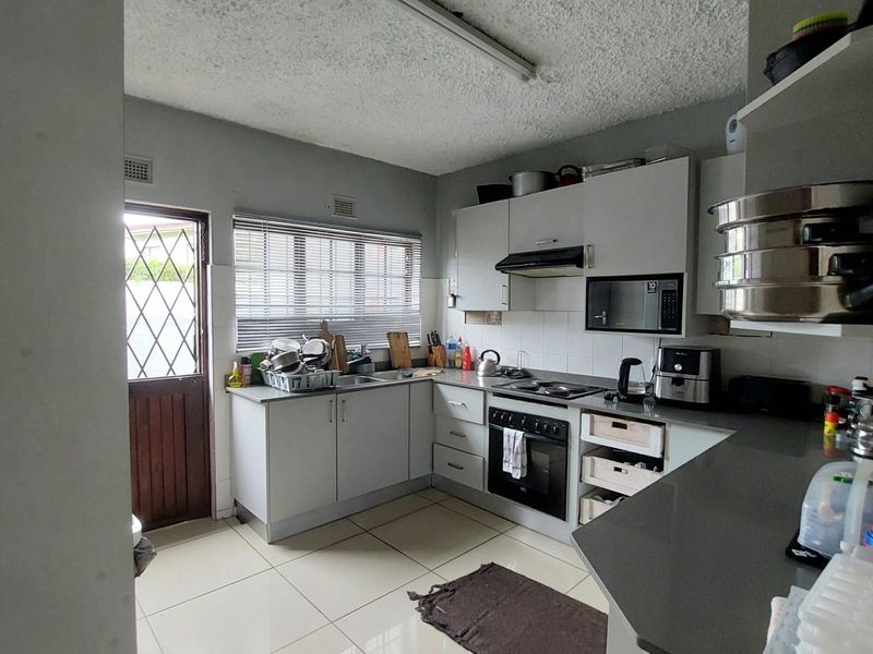 Functional kitchen featuring built-in cabinetry, integrated oven and hob, extractor fan, and tiled flooring with direct access to an exterior door.