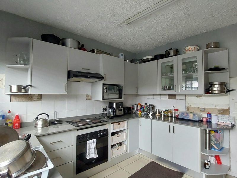 A functional kitchen featuring grey cabinetry, a built-in oven, and hob, requiring some cosmetic attention to wall tiling and plasterwork.