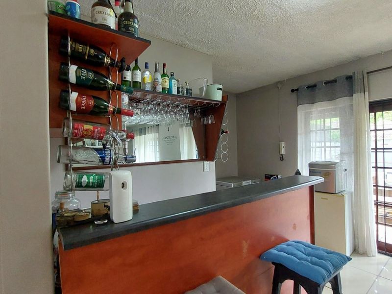 A built-in home bar area featuring a dark countertop, wooden cabinetry, and integrated glass storage, adjacent to a glass sliding door leading outdoors.