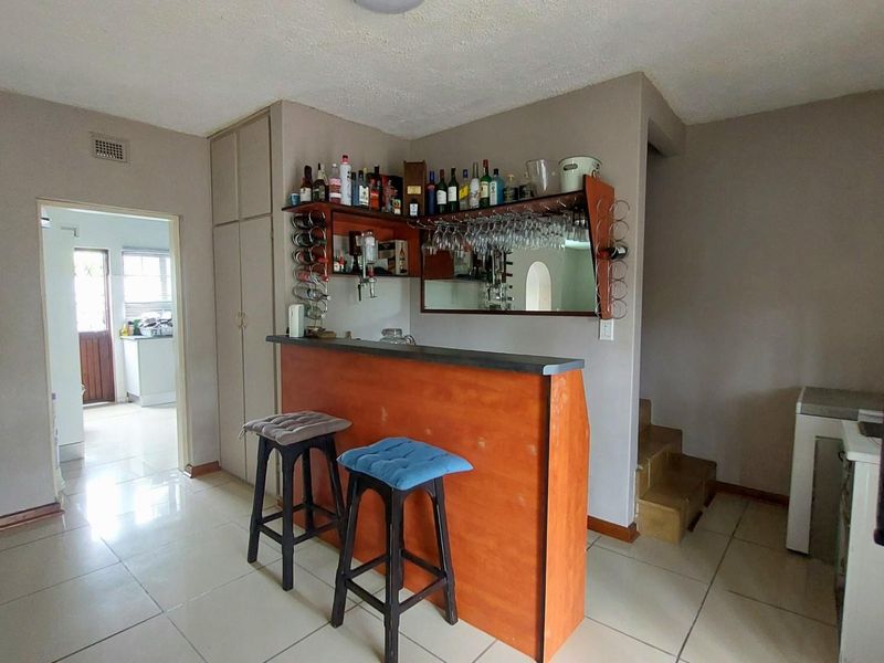 A dedicated bar area featuring a built-in wooden counter, overhead glass storage, and tiled flooring, situated within an open-plan living space.