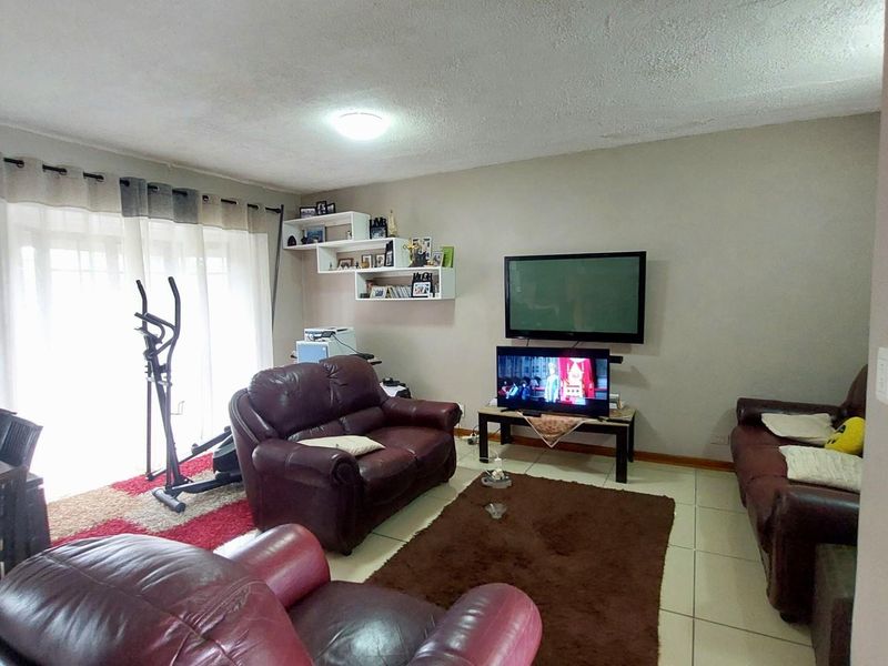 A living room featuring tiled flooring, a wall-mounted television, and sliding glass doors providing access to an outdoor area.