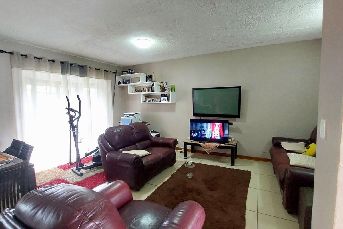 A living room featuring tiled flooring, a wall-mounted television, and sliding glass doors providing access to an outdoor area.
