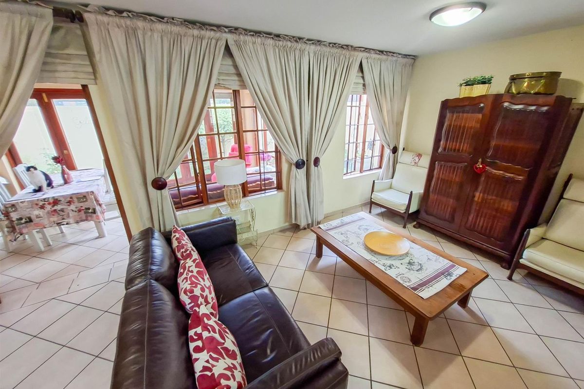 A comfortable living room featuring tiled flooring and large windows with curtains, providing natural light and a view into the adjacent dining area.