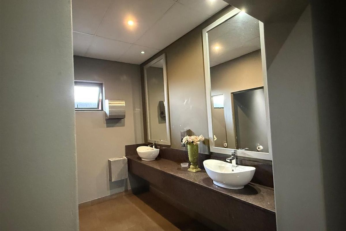Commercial restroom featuring a long vanity with dual vessel sinks, large wall-mounted mirrors, and recessed ceiling lighting.