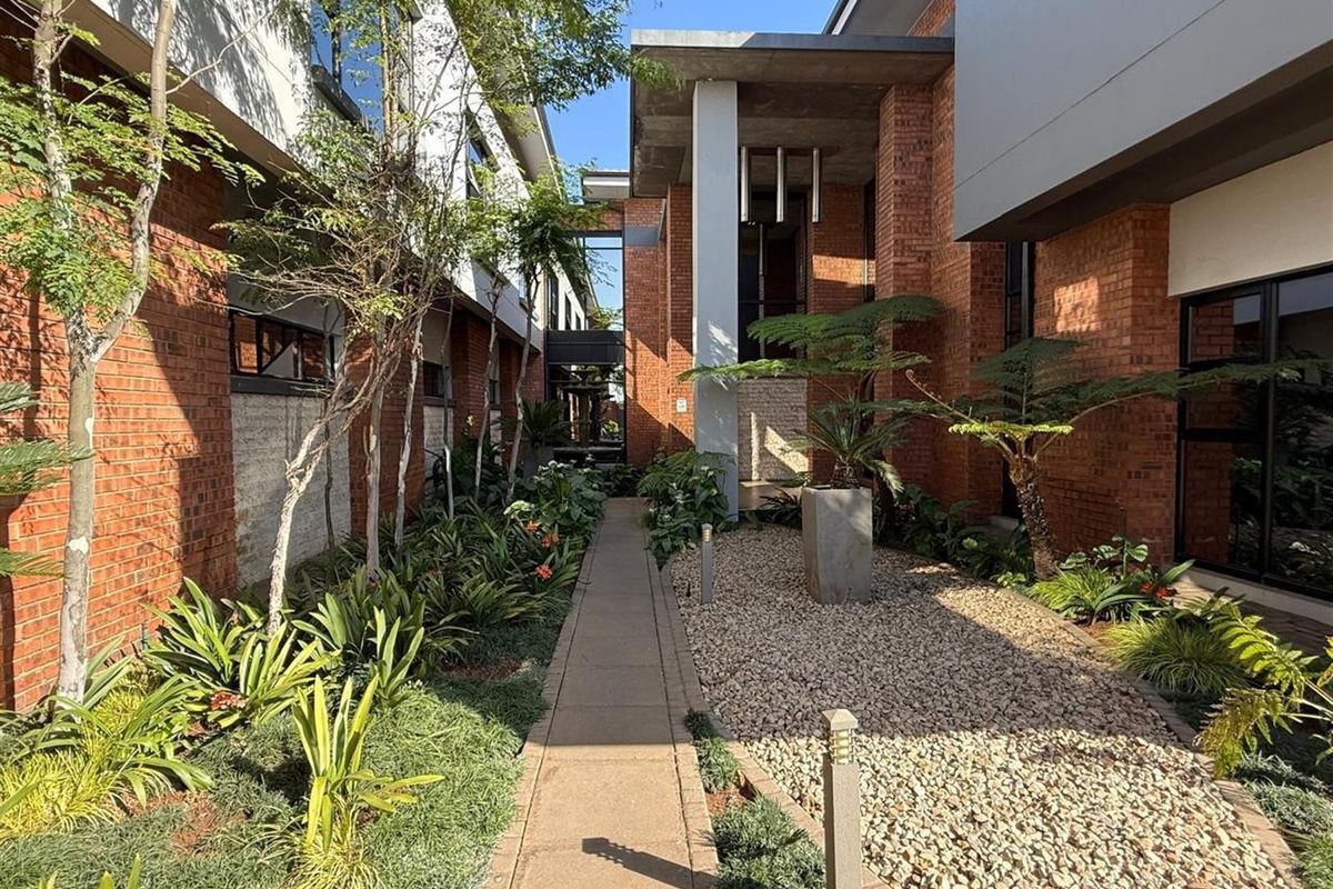 A well-maintained landscaped courtyard featuring a concrete pathway, gravel beds, and exposed brick architectural elements connecting the commercial building wings.