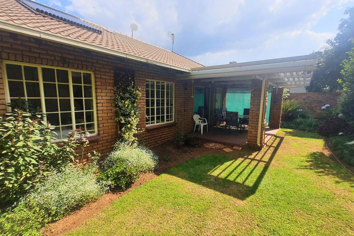 Rear view of the property featuring a brick facade, a covered patio area with a pergola, and a well-maintained garden lawn.