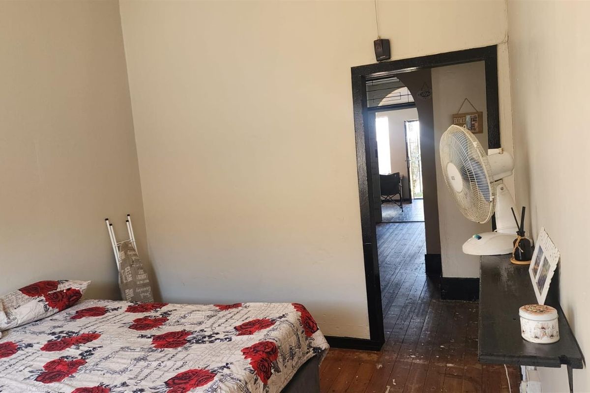 A bedroom featuring original wooden flooring and a doorway leading to an adjacent living space.