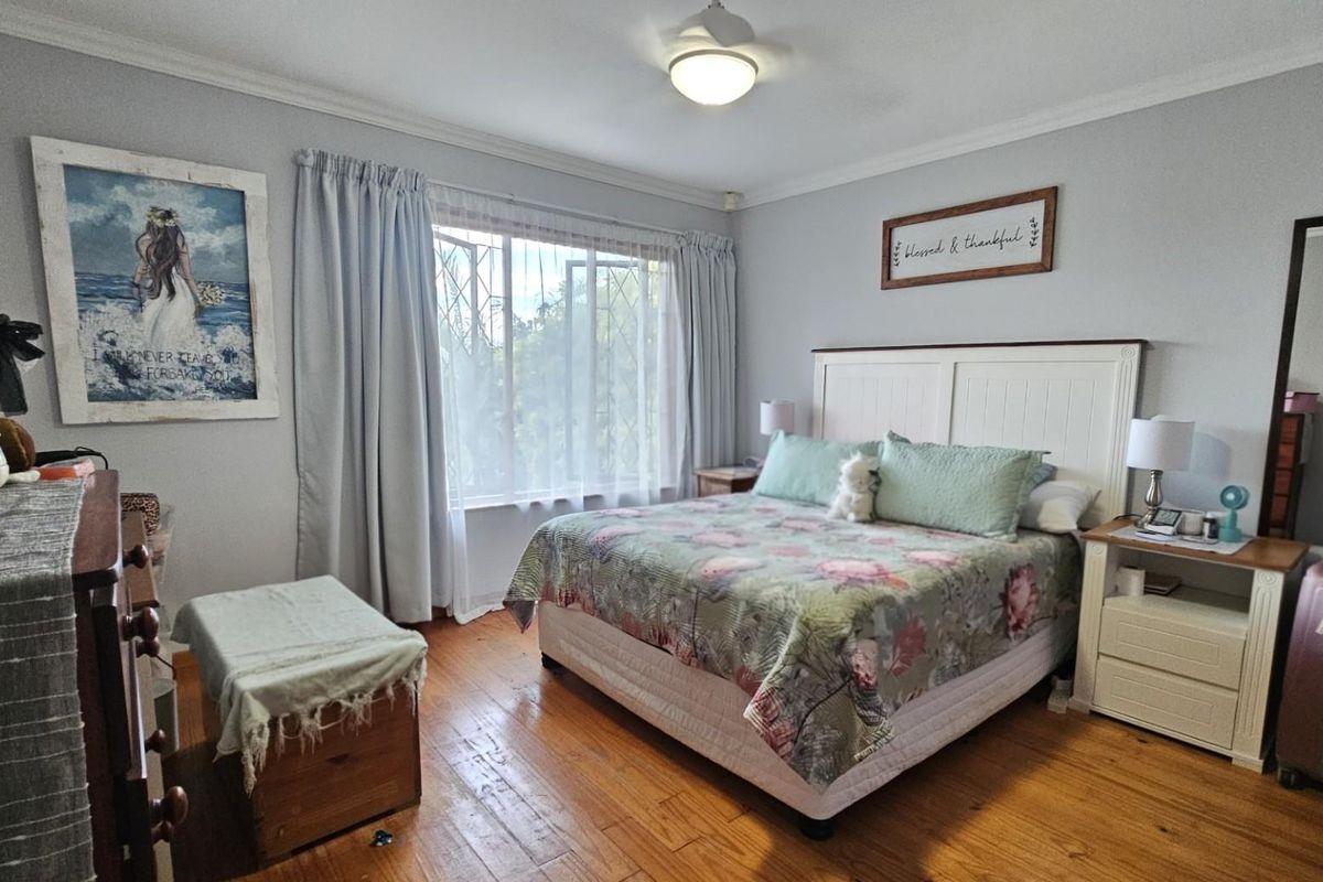 A well-maintained bedroom featuring warm hardwood flooring, a central ceiling fan, and classic cornice detailing, offering a comfortable and inviting living space.