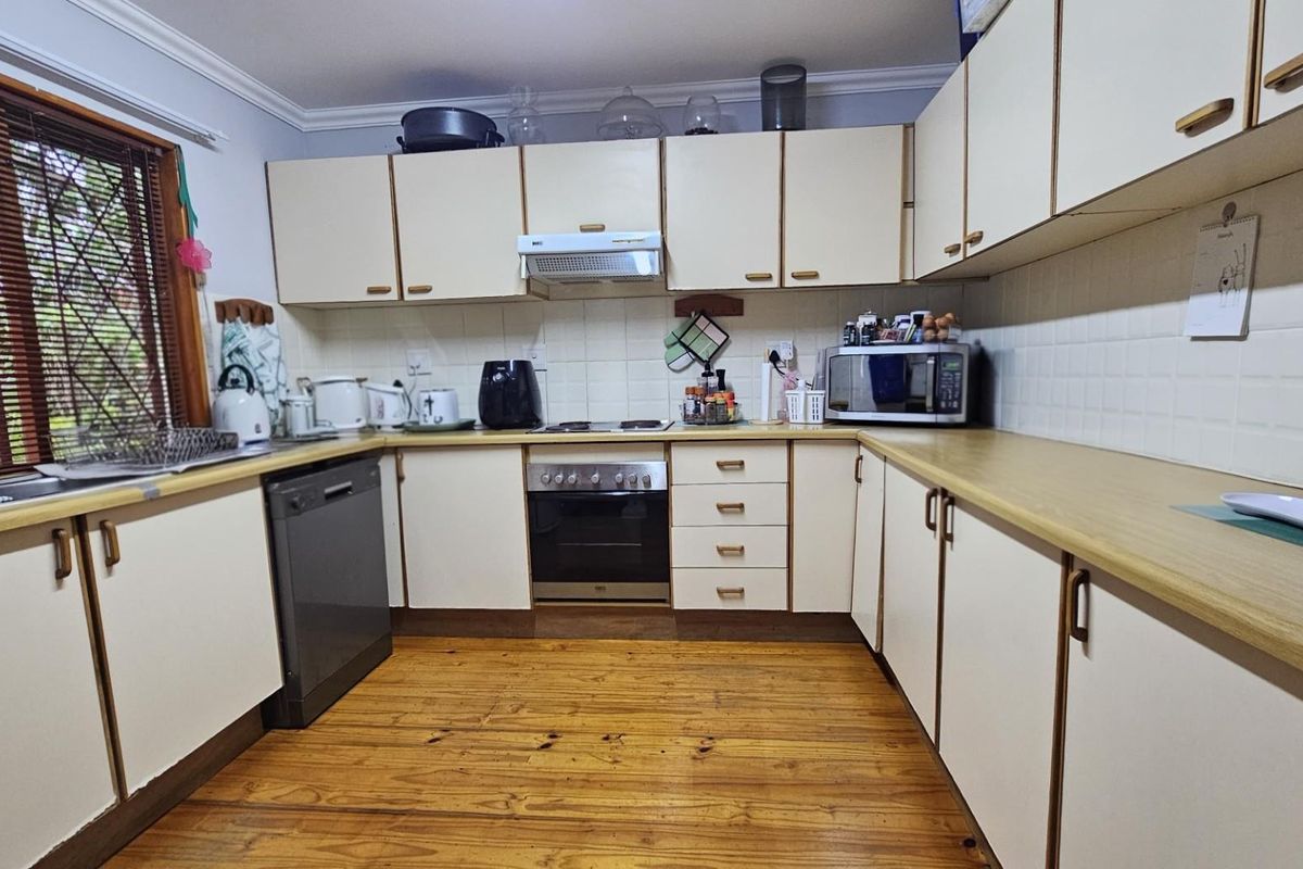 A functional kitchen featuring timber flooring, laminate countertops, built-in cabinetry, and integrated appliances including an oven, hob, and extractor fan.