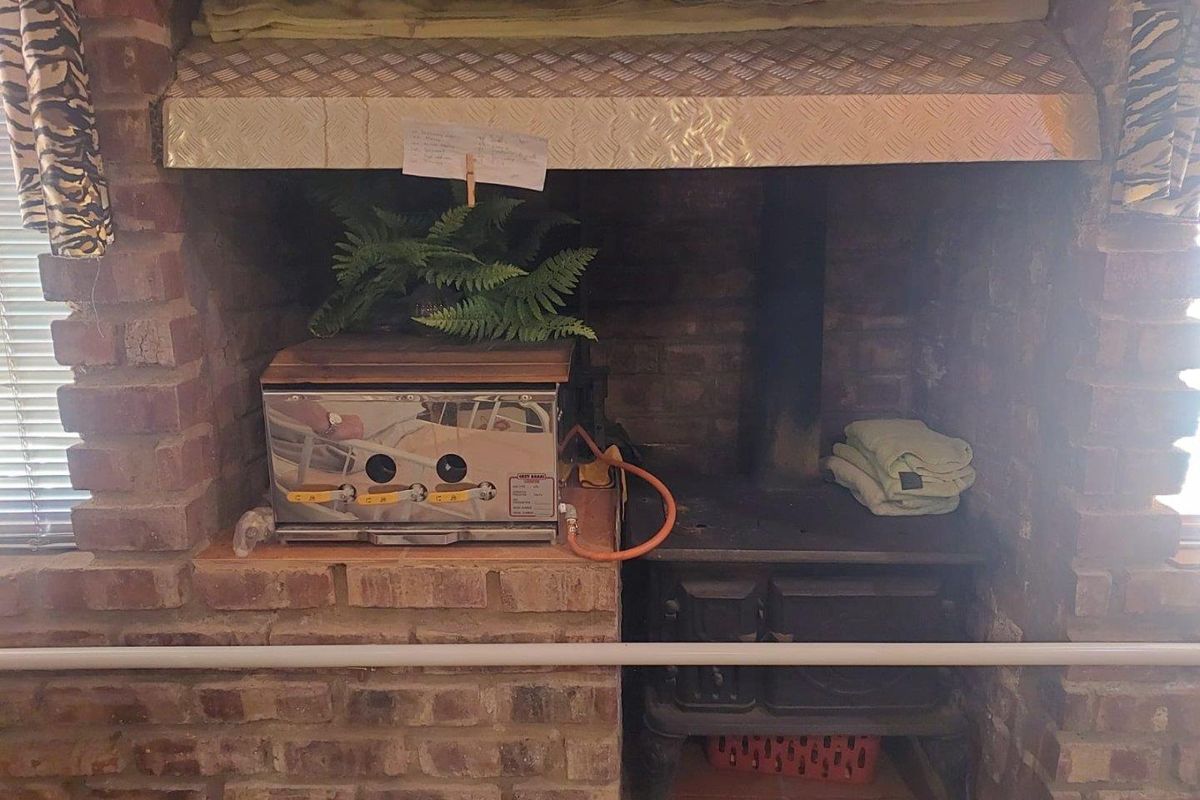 A rustic brick fireplace featuring a built-in hearth, a cast iron wood-burning stove, and a metal extractor hood.