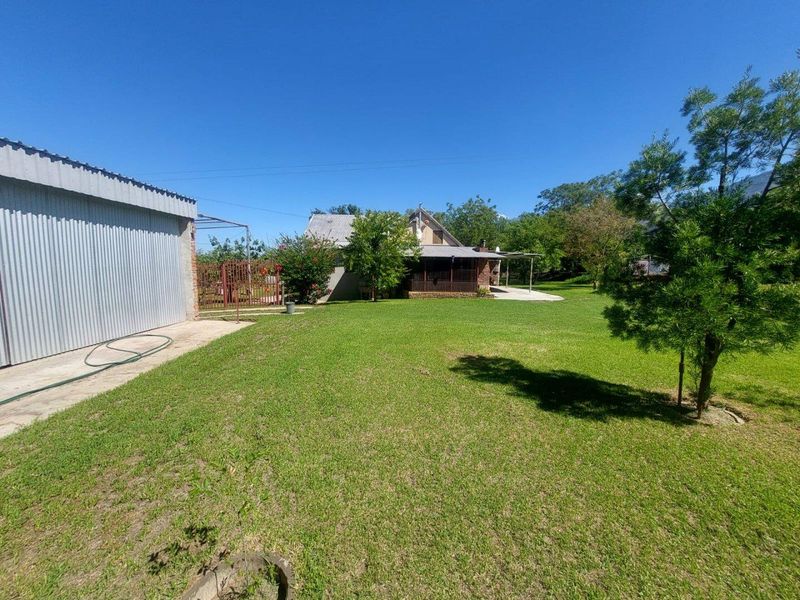 A view of the rear garden and property exterior, featuring a spacious lawn, metal-clad outbuilding, and a covered patio area.