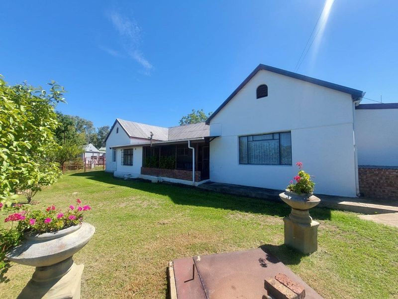 A view of the rear exterior of the farmhouse, featuring a covered patio area, white rendered walls, and a metal roof set within a garden.