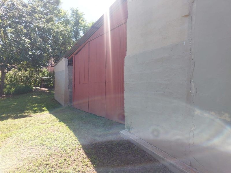 Exterior view of a farm outbuilding featuring corrugated metal siding and masonry walls, set within a grassy garden area.