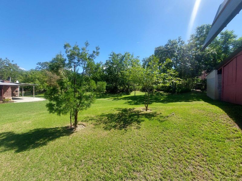 A spacious, well-maintained green lawn area featuring mature trees and a partial view of the property's exterior structures.
