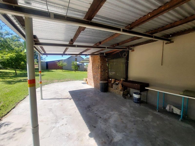 A covered outdoor patio area featuring a brick fireplace structure, concrete flooring, and corrugated metal roofing, overlooking the farm grounds.