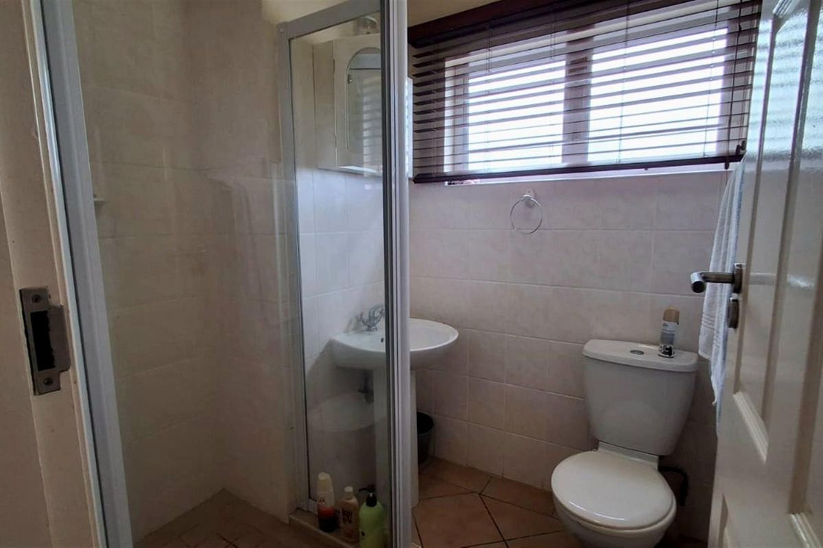 A functional bathroom featuring a glass-enclosed shower, pedestal basin, and toilet, finished with neutral wall tiles and tiled flooring.