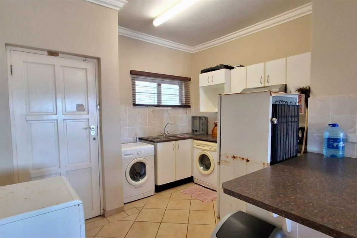 A functional kitchen and laundry area featuring built-in cabinetry, tiled splashbacks, and space for under-counter appliances.