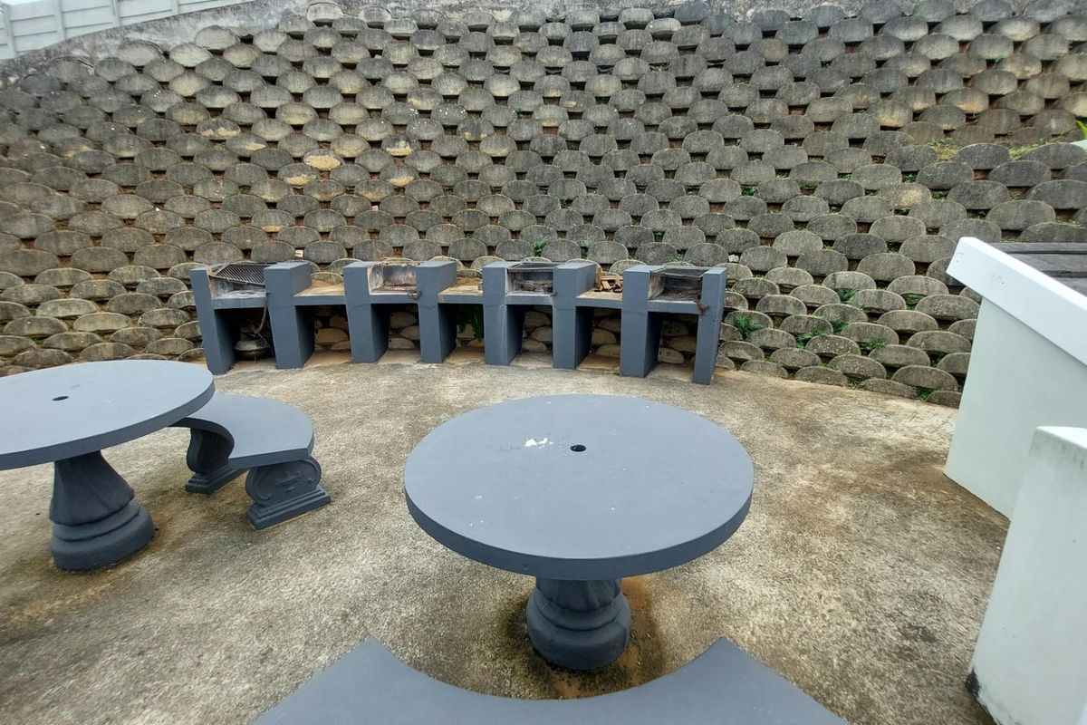 Outdoor communal entertainment area featuring multiple built-in concrete braai stands set against a retaining wall with fixed concrete seating.