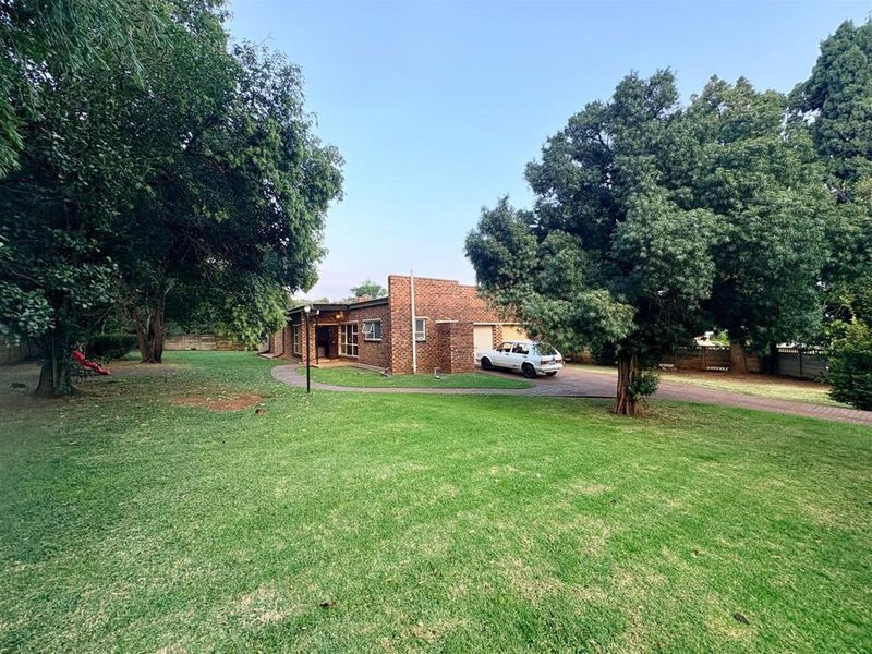 A front view of a brick house featuring a paved driveway, attached garage, and a spacious front lawn with mature trees.
