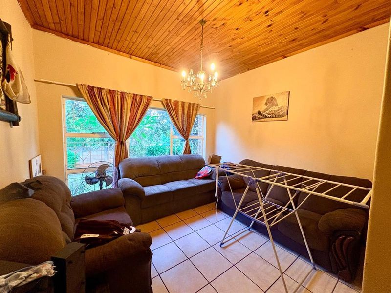 A living room featuring ceramic floor tiles, a timber tongue and groove ceiling, and large aluminium-framed windows.