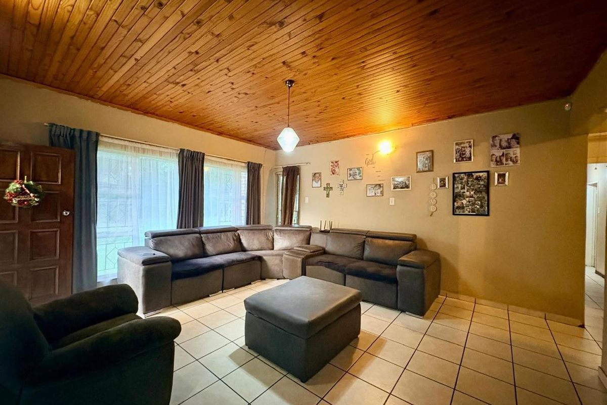 Spacious living room featuring a warm timber tongue and groove ceiling, neutral ceramic floor tiles, and large sliding glass doors for natural light.