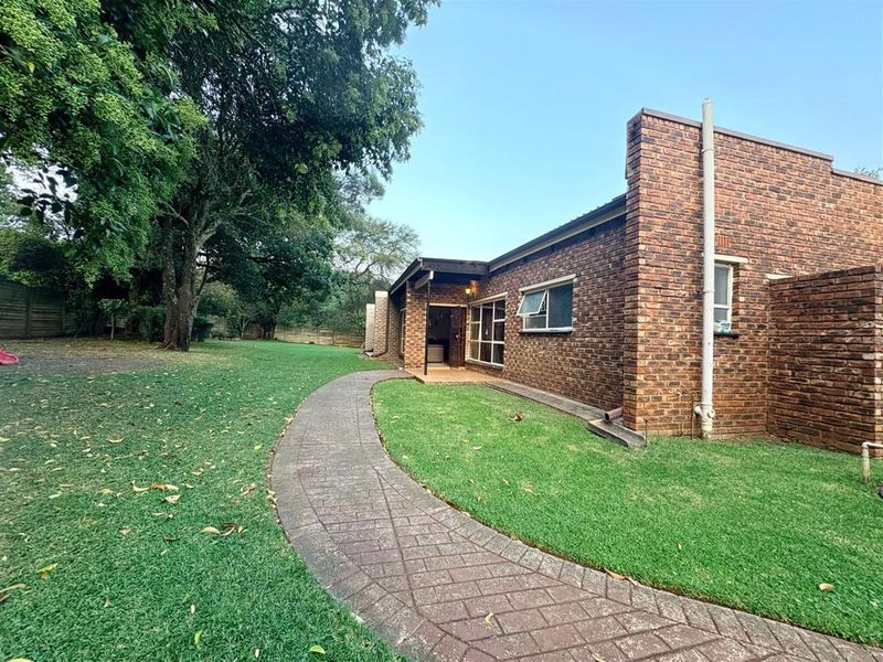 Rear view of the property featuring a face brick facade, a paved walkway leading to a covered patio, and a spacious lawn area.