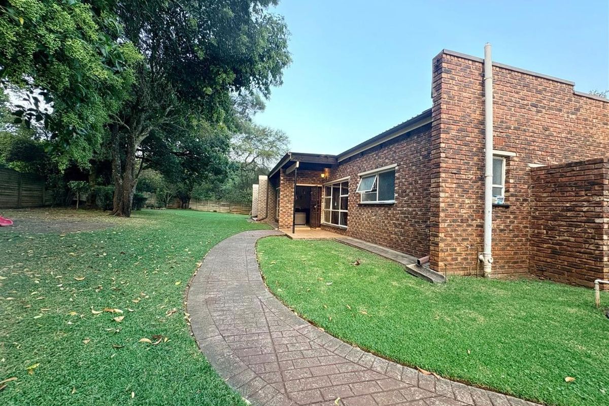Rear view of the property featuring a face brick facade, a paved walkway leading to a covered patio, and a spacious lawn area.