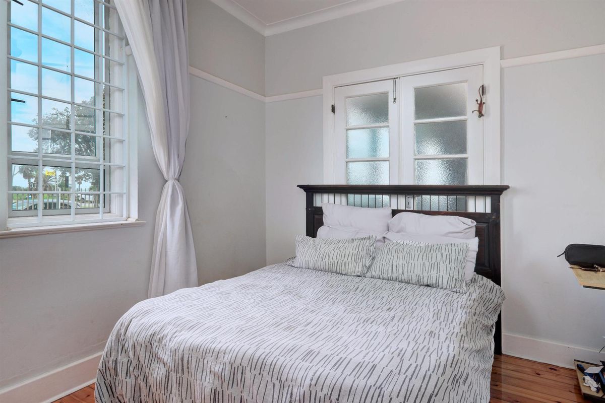 A bedroom featuring polished timber flooring, a large window with security bars, and a classic frosted glass panel door.