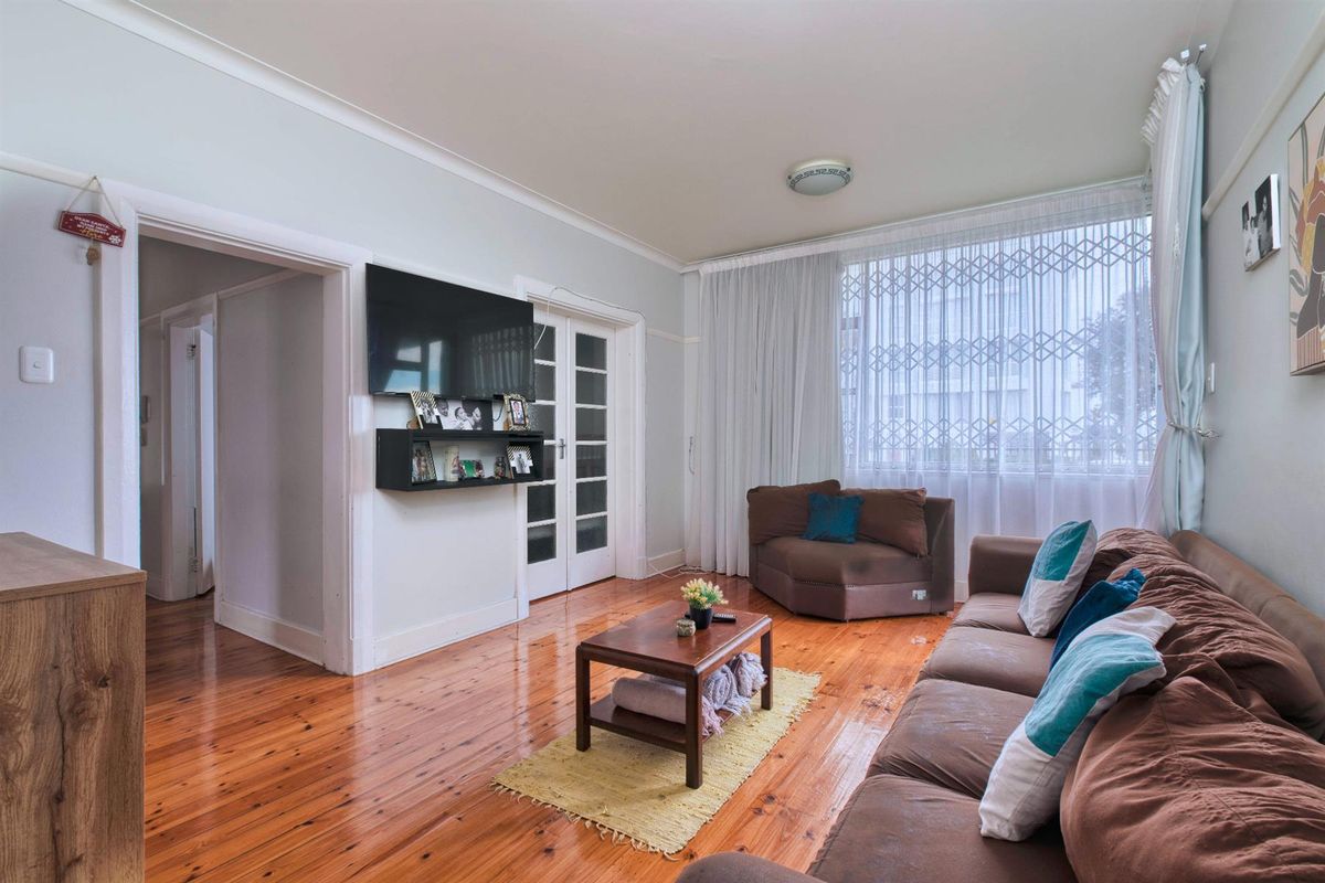 A living room featuring polished hardwood flooring, classic picture rails, and double french doors leading to an adjacent space.