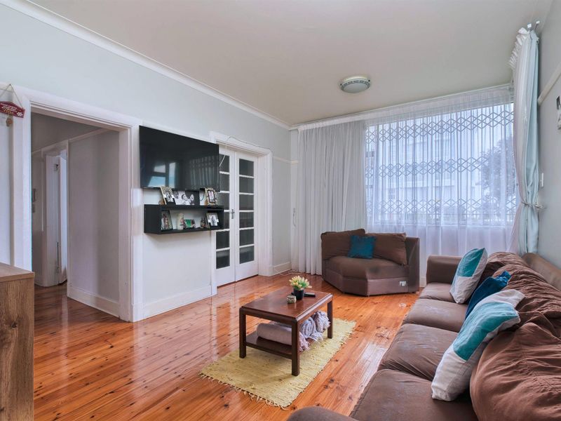 A living room featuring polished hardwood flooring, classic picture rails, and double french doors leading to an adjacent space.