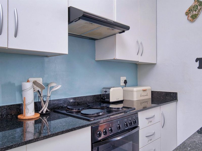 A functional kitchen featuring white cabinetry, dark granite countertops, a built-in electric stove, and a blue tiled backsplash.