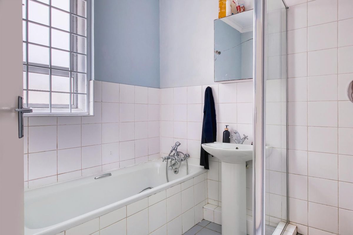 A functional bathroom featuring a bathtub, pedestal basin, and separate shower enclosure with tiled walls and a window with security bars.